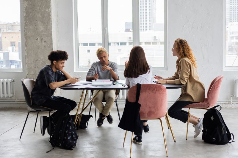 Illustrative stock photograph of four students discussing their work around a table.