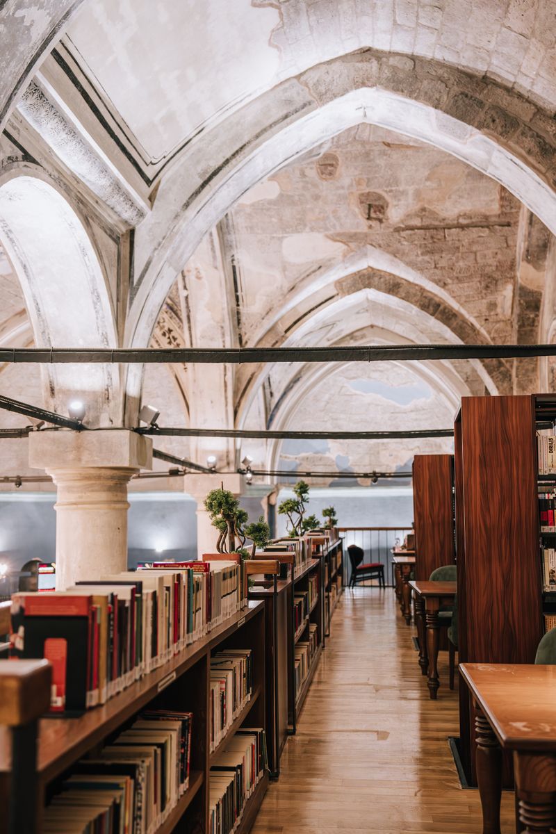 Stock photograph of a sunlit library with stone arches and wooden bookshelves.